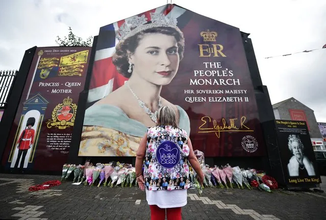 A woman wearing a waistcoat featuring pictures of the Queen is pictured as members of the public leave flowers at a mural of Her Majesty the Queen on the Shankill road on September 9, 2022 in Belfast, United Kingdom. Elizabeth Alexandra Mary Windsor was born in Bruton Street, Mayfair, London on 21 April 1926. She married Prince Philip in 1947 and acceded the throne of the United Kingdom and Commonwealth on 6 February 1952 after the death of her Father, King George VI. Queen Elizabeth II died at Balmoral Castle in Scotland on September 8, 2022, and is succeeded by her eldest son, King Charles III. (Photo by Charles McQuillan/Getty Images)