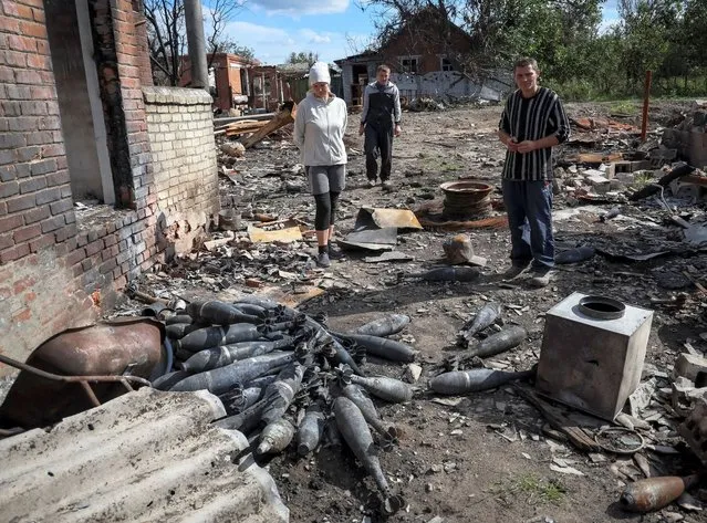 Local residents stand near mortar ammunition at a destroyed street in the village of Kamyanka, recently liberated by Ukrainian Armed Forces, in Kharkiv region, Ukraine on September 22, 2022. (Photo by Gleb Garanich/Reuters)