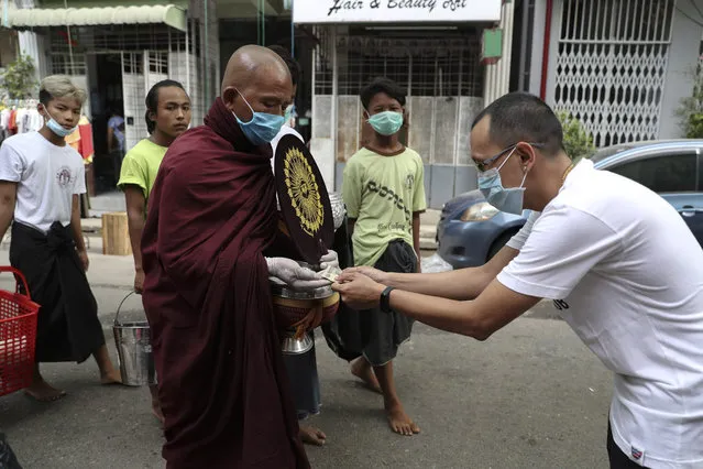 A man donates cash to a Buddhist monk wearing face mask and gloves as they collect morning alms in a street in Yangon, Myanmar, Wednesday, April 8, 2020. (Photo by Thein Zaw/AP Photo)