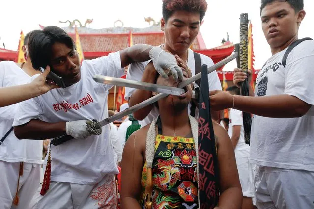 A man speaks on a mobile phone as he puts another sword through a cheek of a devotee of the Chinese Bang Neow Shrine before a procession celebrating the annual vegetarian festival in Phuket September 29, 2014. (Photo by Damir Sagolj/Reuters)