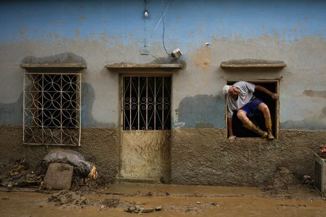 Jose Medina jumps out his home flooded by the overflow of a ravine caused by intense rains in Las Tejerias, Venezuela, Sunday, October 9, 2022. (Photo by Matias Delacroix/AP Photo)