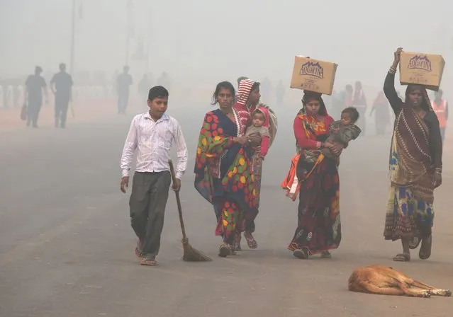 Indian residents walk along a road amid heavy smog in New Delhi on November 9, 2017. Rickshaw driver Sanjay can only afford a handkerchief to shield his face as he weaves through the smog-filled streets of Delhi amid a rush on protection against the toxic menace. Better off residents of the global pollution black spot are swarming sellers of face masks – that cost more than the 300 rupees ($5) that Sanjay earns in a day – and high-tech air purifiers that could easily cost a year of his wage. (Photo by Dominique Faget/AFP Photo)