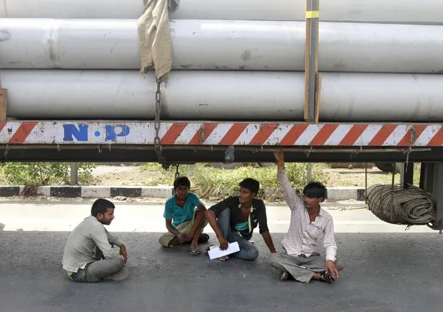 Truck drivers and helpers sit under a parked truck while waiting to get their loads cleared to cross a checkpoint at the Commercial Taxes Department check post at Walayar in Palakkad district in southern Indian state of Kerala, India, September 5, 2015. (Photo by Sivaram V/Reuters)