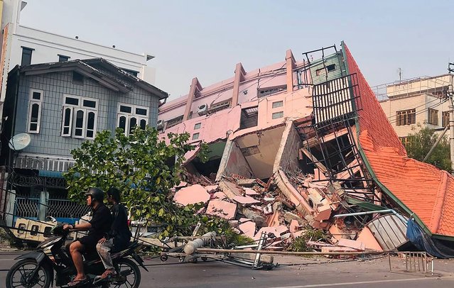 People drive on a motorbike past a collapsed building in Mandalay on March 28, 2025, after an earthquake in central Myanmar. (Photo by AFP Photo/Stringer)