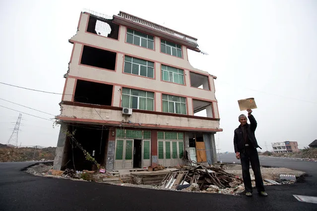 Luo Baogen holds his land certificate as he stands next to his house in the middle of a newly built road in Wenling city in east China's Zhejiang province Thursday, November 22, 2012. Luo, the owner of the house, refused to sign an agreement to allow his house to be demolished by the authorities, as the compensation offered to him was not enough, according to local media. (Photo by AP Photo)