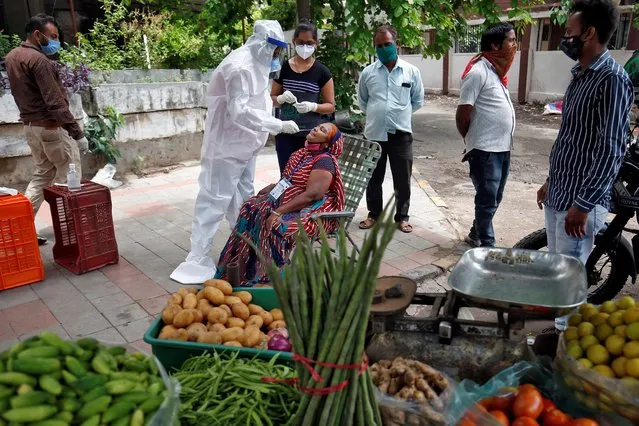 A healthcare worker wearing personal protective equipment (PPE) takes a swab from a vegetable vendor to test her for the coronavirus disease (COVID-19) at a roadside market in Ahmedabad, India, July 7, 2020. (Photo by Amit Dave/Reuters)