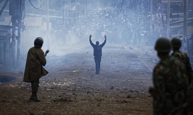 A man seeking safety walks with his hands in the air through a thick cloud of tear gas toward riot police, as they clash with protesters throwing rocks in the Kawangware slum of Nairobi, Kenya on August 10, 2017. International observers urged Kenyans to be patient as they awaited final election results following opposition allegations of vote-rigging, but clashes between police and protesters again erupted in Nairobi. (Photo by Ben Curtis/AP Photo)