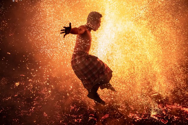 Balinese man jumps into the fire of burn coconut husks during the fire ritual on March 10, 2024 at traditional sub village of Nagi, in Gianyar, Bali, Indonesia. The mesabatan api ritual is held annually on the eve of Nyepi, the Hindu Day of Silence, the Balinese Caka New Year. The community in Pakraman Nagi village believe the mesabatan api ritual is a part of the cleansing the negative power on their self. Two groups of young men will be busy burning piles of dry coconut husks burst into flames, sending dozens of bare-breasted young men with headdresses and checkered cloths scurrying and kicking the burning husks. The group will bare-handedly grab two blazing coconut husks and threw them at their enemies, hitting them in the back. Others immediately took revenge, aiming at their opponents' faces. The celebration of the Nyepi festivities for Balinese Hindus in Indonesia, as the opportunity for self-reflection which is called mulat sarira. All the resident and visitors required to abide by the rules called Catur Brata Penyepian consist of amati geni (no open fires or flames), amati lelanguan (no pleasurable activities), amati karya (no work or labor) and amati lelungan (no journeys). (Photo by Agung Parameswara/Getty Images)
