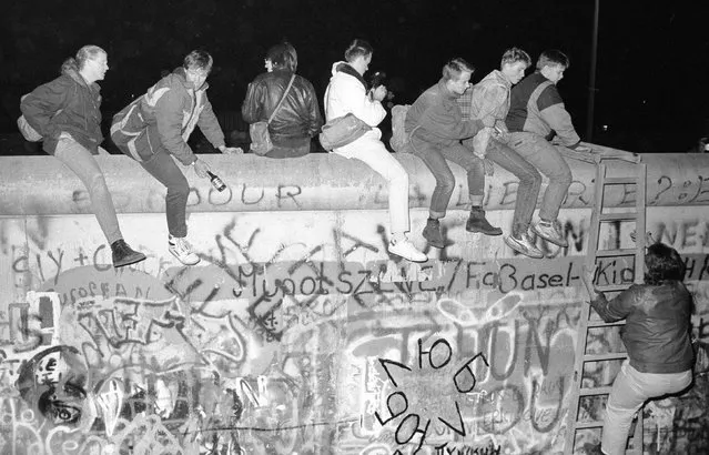 West German citizens sit on the top of the Berlin wall near the Allied checkpoint Charlie after the opening of the East German border was announced November 9, 1989. (Photo by Fabrizio Bensch/Reuters)