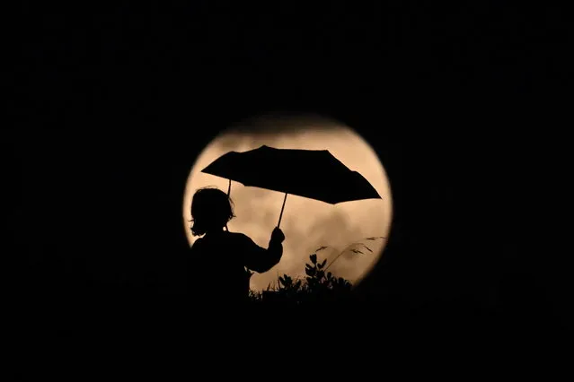 A child plays with an umbrella against the rising full moon ahead of a total lunar eclipse in Stanwell Park, Australia, 08 November 2022. A blood moon will be visible when a total lunar eclipse takes place later tonight. (Photo by Dean Lewins/EPA/EFE)