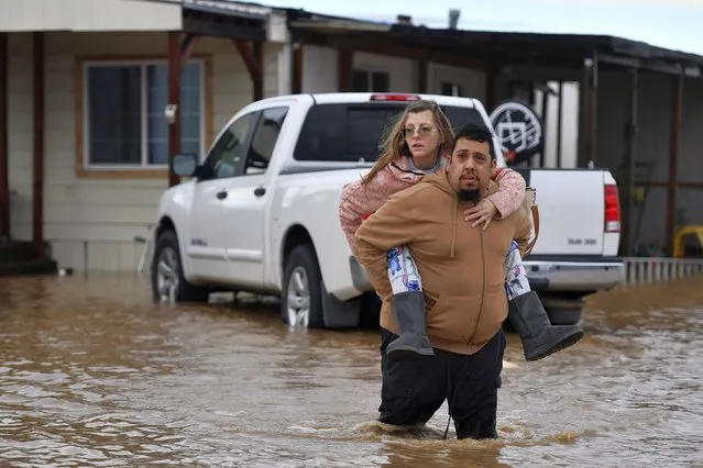 Ryan Orosco, of Brentwood, carries his wife Amanda Orosco, from their flooded home on Bixler Road in Brentwood, Calif., on Monday, January 16, 2023. The last in a three-week series of major winter storms is churning through California. (Photo by Jose Carlos Fajardo/Bay Area News Group via AP Photo)