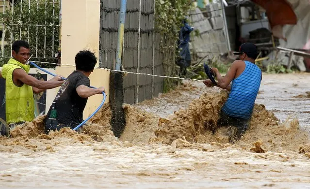 Residents hold on to a plastic hose and an electricity wire while trying to cross a flooded road amidst a strong current in Sta Rosa, Nueva Ecija in northern Philippines, October 19, 2015, after it was hit by Typhoon Koppu. (Photo by Erik De Castro/Reuters)