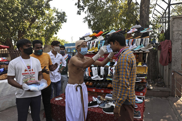 A boy dressed as Mahatma Gandhi puts a face mask on a roadside vendor during a COVID-19 awareness campaign on the birth anniversary of the independence leader, in New Delhi, India, Friday, October 2, 2020. (Photo by Manish Swarup/AP Photo)