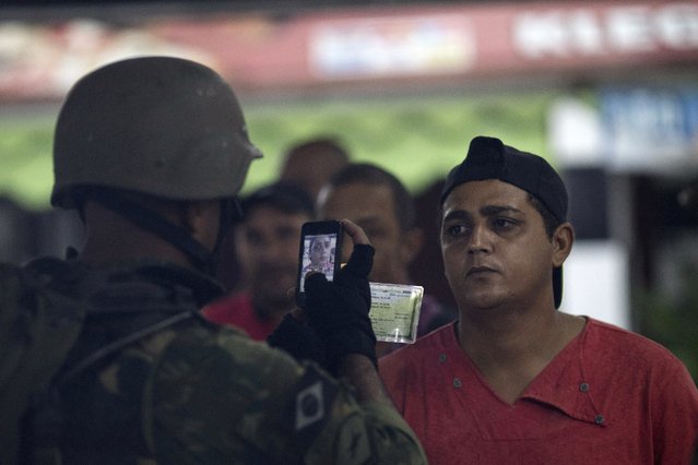 In this Friday, February 23, 2018 photo, a soldier takes a picture of a resident and his identification card during a surprise operation at the Vila Kennedy slum in Rio de Janeiro, Brazil. Michel Temer's presidential decree to put the military in charge of Rio's security forces has caused unease in Brazil, where many still remember the 1964-1985 military regime. (Photo by Leo Correa/AP Photo)