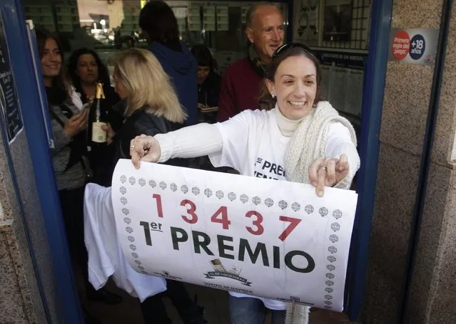 Lottery seller Raquel Carrasco holds a sign with the winning number of Spain's Christmas Lottery “El Gordo”, in La Eliana near Valencia December 22, 2014. (Photo by Heino Kalis/Reuters)