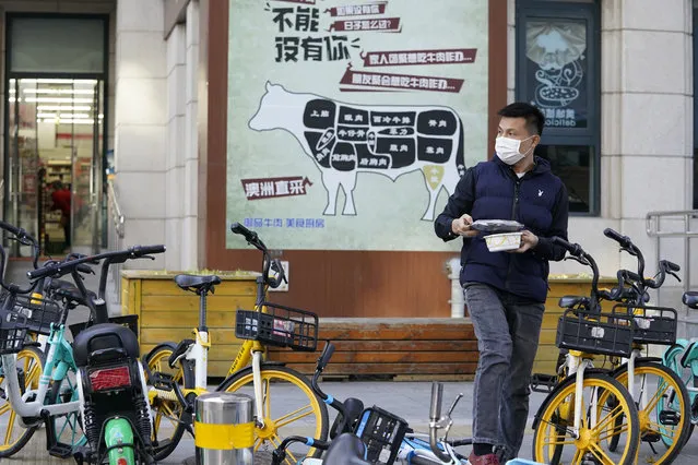 A man carries his meal past an advertisement promoting imported beef from Australia in Beijing, Monday, November 23, 2020. China has stirred controversy with claims it has detected the coronavirus on packages of imported frozen food. (Photo by Ng Han Guan/AP Photo)