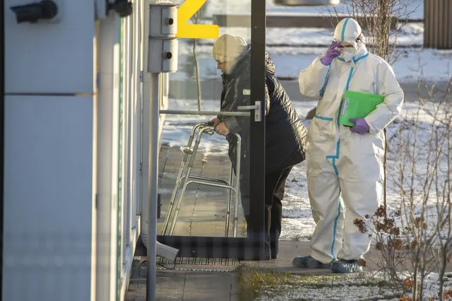 A medical worker wearing protective gear escorts a woman, suspected of having coronavirus, at a hospital in Kommunarka, outside Moscow, Russia, Saturday, December 5, 2020. (Photo by Pavel Golovkin/AP Photo)