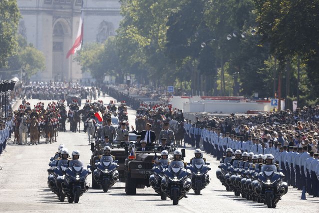 France's President Emmanuel Macron (centre L) waves in the command car with Chief of Staff of the Armed Forces (CEMA), Thierry Burkhard during the Bastille Day military parade on the Avenue Foch, with the Arc de Triomphe in the background in Paris on July 14, 2024. (Photo by Ludovic Marin/Pool via AFP Photo)