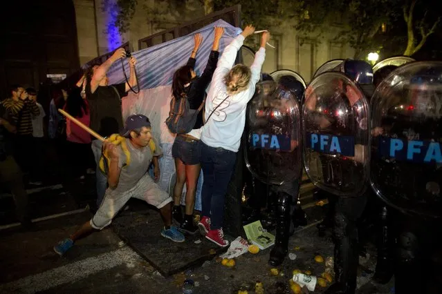 A demonstrator hits riot police as women hang an Argentine flag on a barrier during a protest sparked by the death of special prosecutor Alberto Nisman outside the government house in Plaza de Mayo in Buenos Aires, Argentina, Monday, January 19, 2015. (Photo by Rodrigo Abd/AP Photo)