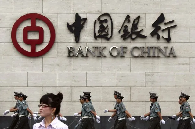 A woman stands on a street as security guards march behind her outside the Bank of China headquarters in the financial district of Beijing in this August 19, 2009 file photo. China's central bank cut the amount of cash that banks must hold as reserves on Wednesday, the first industry-wide cut in more than 2-1/2 years, as it increased efforts to shore up flagging growth in the world's second-largest economy. (Photo by David Gray/Reuters)