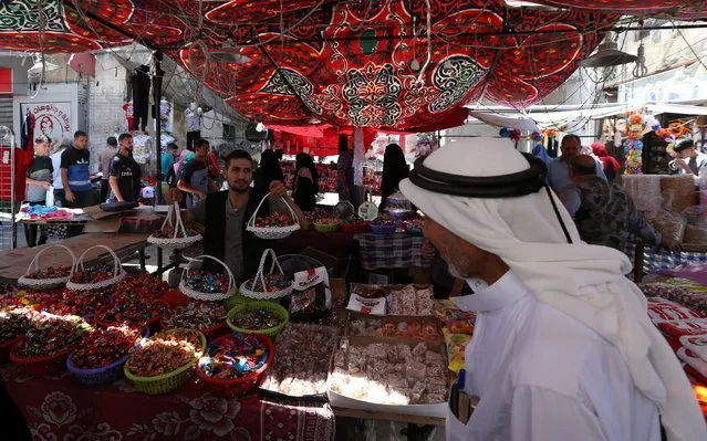 A vendor sells sweets as Palestinians shop in a market ahead of the upcoming Eid al-Fitr holiday marking the end of the Muslim holy month of Ramadan, in Rafah in the southern Gaza Strip June 14, 2018. (Photo by Ibraheem Abu Mustafa/Reuters)