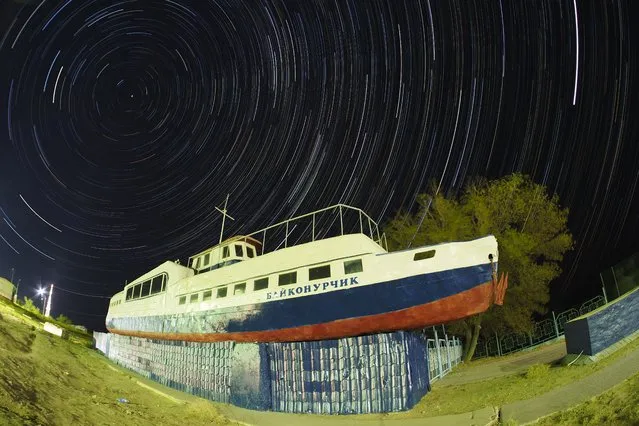 In this photo taken with a long exposure, stars move in an arc around the Polar Star over a river boat used as a cafe at the Russian leased Baikonur cosmodrome, Kazakhstan, Sunday, September 18, 2022. The new Soyuz mission to the International Space Station (ISS) is scheduled on Wednesday, Sept. 21 with NASA astronaut Frank Rubio, along with Roscosmos cosmonauts Sergey Prokopyev and Dmitri Petelin. (Photo by Dmitri Lovetsky/AP Photo)