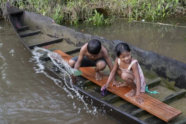 Indigenous Wari' children throw out water from a boat in the Komi Memem River, named Laje in non-Indigenous maps, in Guajara-Mirim, Rondonia state, Brazil, Friday, July 14, 2023. The Amazon city of Guajara-Mirim recently approved a law that designates the river “as a living entity and subject to rights”. (Photo by Andre Penner/AP Photo)