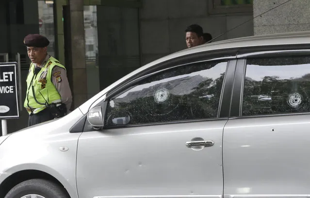 A police officer walks past a car with bullet holes on its windows outside the Starbucks cafe where Thursday's attack occurred in Jakarta, Indonesia, Friday, January 15, 2016. Indonesians were shaken but refusing to be cowed a day after a deadly attack in a busy district of central Jakarta that has been claimed by the Islamic State group. (Photo by Tatan Syuflana/AP Photo)