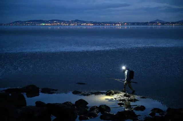 A man wearing a head torch carries his fishing rod for night time fishing on Poolbeg beach along Great South Wall pier as the tide comes in, amid the spread of the coronavirus disease (COVID-19), in Dublin, Ireland, March 15, 2021. (Photo by Clodagh Kilcoyne/Reuters)