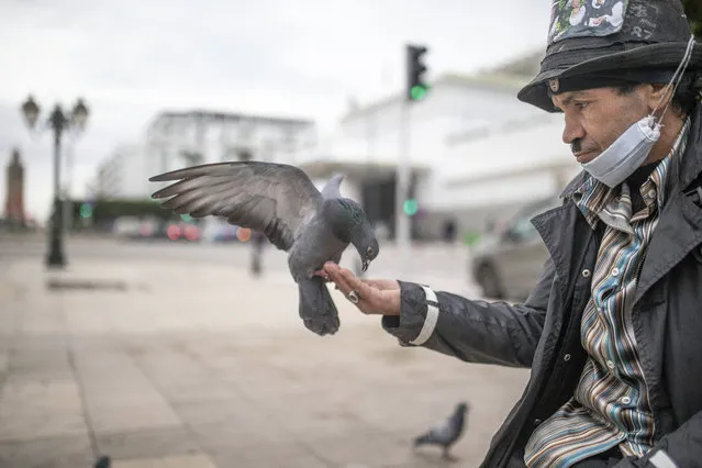 Belhussein Abdelsalam, 58, a Charlie Chaplin impersonator feeds pigeons as he waits for customers in one of the main avenues in Rabat, Morocco, Wednesday, December 16, 2020. When 58-year-old Moroccan Belhussein Abdelsalam was arrested and lost his job three decades ago, he saw Charlie Chaplin on television and in that moment decided upon a new career: impersonating the British actor and silent movie maker remembered for his Little Tramp character. (Photo by Mosa'ab Elshamy/AP Photo)