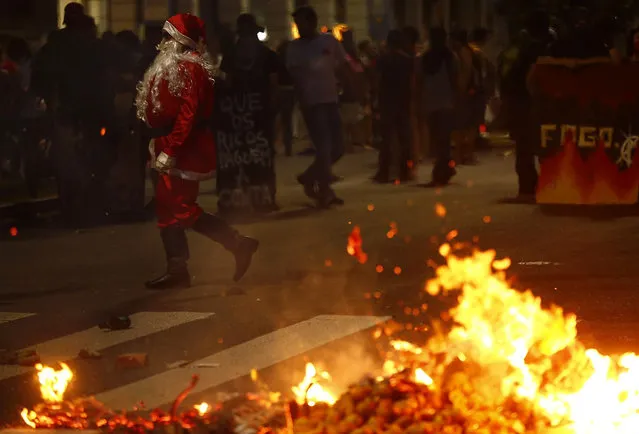 A demonstrator dressed as Santa claus walks next to a barricade burned by anti-government demonstrators during a protest against the constitutional amendment PEC 55, which limits public spending, in Porto Alegre, Brazil December 13, 2016. (Photo by Lunae Parracho/Reuters)