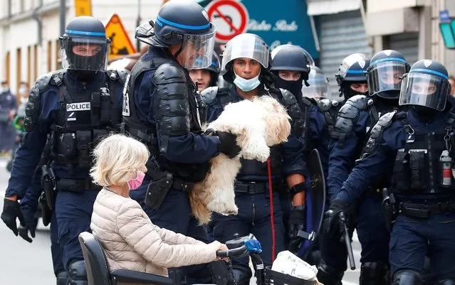 A police officer helps a woman with a dog during a protest against the new measures announced by French President Emmanuel Macron to fight the coronavirus disease (COVID-19) outbreak, in Paris, France, July 14, 2021. (Photo by Gonzalo Fuentes/Reuters)