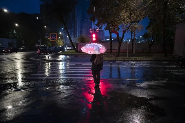 A pedestrian holds an umbrella as he waits for a green traffic light on an almost empty street during an autumn rain in Moscow, Russia, Tuesday, September 21, 2021. The temperature in Moscow dropped to about 7 degrees (44,6 degrees Fahrenheit). (Photo by Alexander Zemlianichenko/AP Photo)