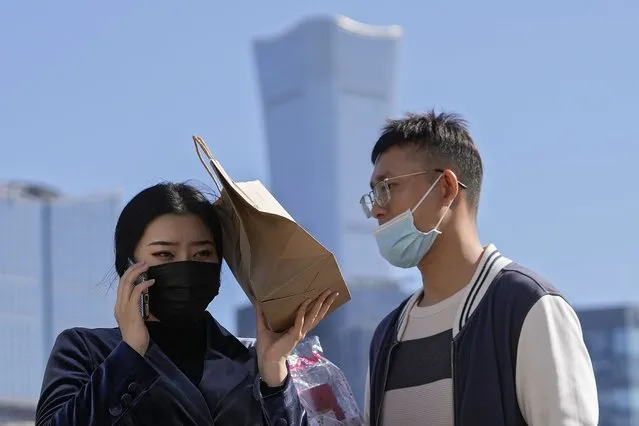 A man and a woman wearing face masks to help curb the spread of the coronavirus, walk across an intersection against the Central Business District in Beijing, Tuesday, October 12, 2021. (Photo by Andy Wong/AP Photo)