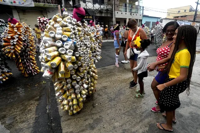 Locals watch revelers wearing costumes made from beer and soda cans during the “Bloco da Latinha” street party Carnival parade in Madre de Deus, Brazil, Sunday, February 11, 2024. (Photo by Eraldo Peres/AP Photo)