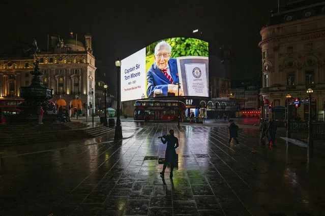 A woman plays the violin as a tribute to Captain Sir Tom Moore is displayed in Piccadilly Circus, London, Tuesday, February 2, 2021. The British World War II veteran who walked into the hearts of a nation in lockdown as he shuffled up and down his garden to raise money for health care workers has died after testing positive for COVID-19. Capt. Tom Moore was 100-years-old. (Photo by Aaron Chown/PA via AP Photo)