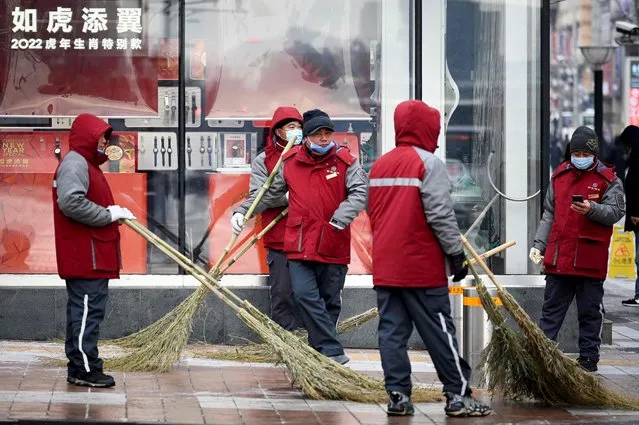A group of workers prepare to sweep the snow along a street in Beijing on January 20, 2022. (Photo by Wang Zhao/AFP Photo)