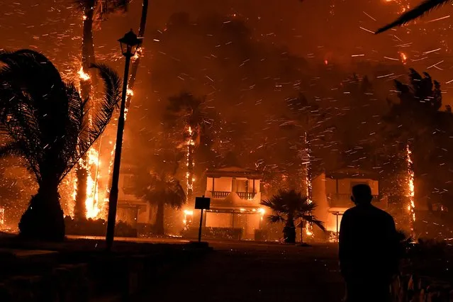 A local resident looks at flames rising among houses as a wildfire burns in the village of Schinos, near Corinth, Greece, May 19, 2021. Greek authorities moved more people to safety on Thursday as firefighters battled a forest fire that spread from the Corinth region of southern Greece to western Attica, they said. (Photo by Vassilis Psomas/Reuters)