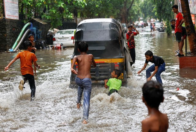 A boy clings to an auto rickshaw on a waterlogged street after heavy rains in Mumbai, India on July 8, 2024. (Photo by Francis Mascarenhas/Reuters)