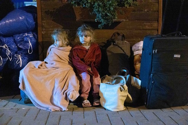 Children huddle up for warmth as they try to sleep on the pavement with their belongings in the Hungarian town of Kocs, about 70 kilometers west of Budapest, on August 22, 2024. They were evicted from a privately owned shelter after a Hungarian government directive limited free shelter to refugees from conflict-affected regions of Ukraine. (Photo by Radio Free Europe/Radio Liberty)