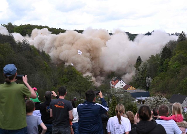 People take pictures of the Rahmede highway bridge during its blasting on May 7, 2023 on the A45 motorway, near Luedenscheid, western Germany. During a routine inspection of the 453-metre-long Rahmede viaduct in December 2021, inspectors discovered deformations in the steel wall that could affect the bridge's load-bearing capacity. According to the motorway company, a new construction will take at least five years. (Photo by Ina Fassbender/AFP Photo)