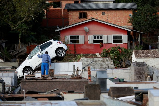 A man stands next to a car which came to rest on top of graves at the Pedro Freiberger cemetery as a result of flooding due to heavy rains following an extratropical cyclone, in Caraa, Rio Grande do Sul state, Brazil on June 18, 2023. (Photo by Diego Vara/Reuters)