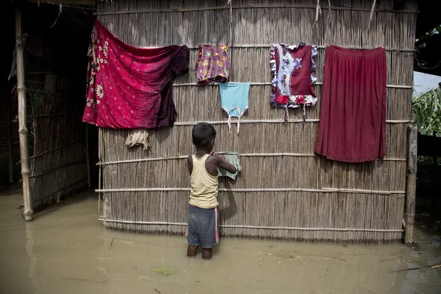 An Indian boy dries clothes outside his house, partially submerged in flood waters at Burgaon, 80 kilometers (50 miles) east of Gauhati, Assam state, India, Wednesday, July 5, 2017. Heavy rains since the start of India's monsoon season have triggered floods and landslides in parts of the remote northeastern region, causing at least 20 deaths, authorities said Wednesday. (Photo by Anupam Nath/AP Photo)