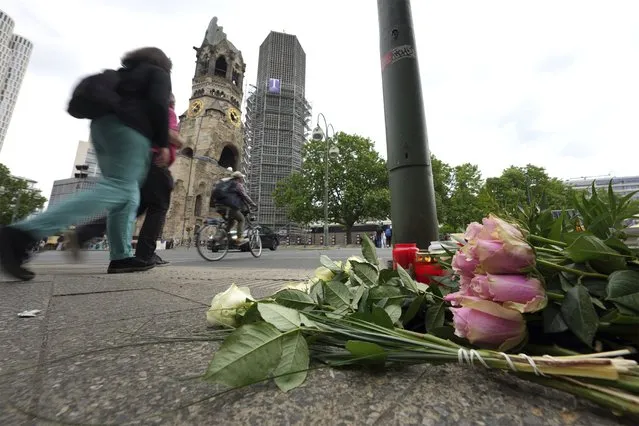 People walk past flowers and candles at the Kaiser Wilhelm Memorial Church in Berlin, Germany, Thursday, June 9, 2022. On Wednesday June 8, a 29-year-old man drove his car into a group of students killing their teacher and crash into a store. (Photo by Michael Sohn/AP Photo)