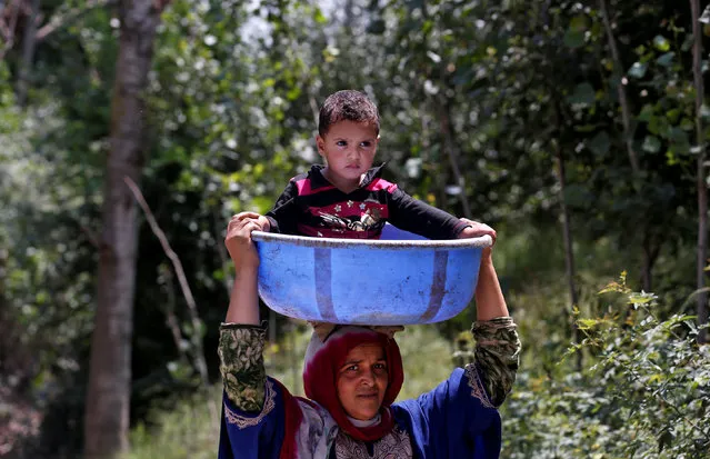 A woman carries a child in a plastic container through a road at Tantray Pora in south Kashmir's Kulgam district August 3, 2017. (Photo by Danish Ismail/Reuters)