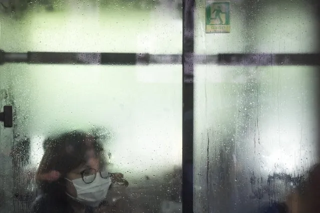 A woman wearing a face mask looks through a fogged-up window on a public bus during a rainy morning in the central business district in Beijing, Tuesday, July 12, 2022. (Photo by Mark Schiefelbein/AP Photo)