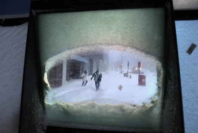 Jennifer Rice and Mike Femia battle wind-driven snow as they make their way to their jobs at a pharmaceutical lab, as seen through a window, Tuesday, January 27, 2015, in downtown Portland, Maine. (Photo by Robert F. Bukaty/AP Photo)