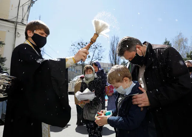 A clergyman wearing a protective face mask sprinkles holy water on believers during a ceremony to bless Easter cakes and eggs on the eve of the Orthodox Easter, amid the coronavirus disease (COVID-19) outbreak in Stavropol, Russia on April 18, 2020. (Photo by Eduard Korniyenko/Reuters)