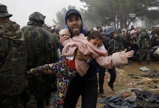 A Syrian refugee carries a child as he walks through the mud to cross the border from Greece into Macedonia during a rainstorm, near the Greek village of Idomeni, September 10, 2015. (Photo by Yannis Behrakis/Reuters)