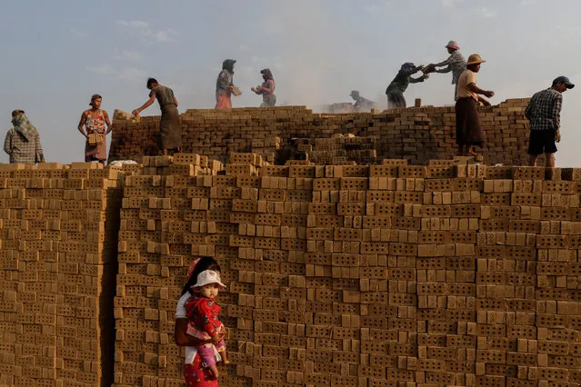 A girl carrying a child walks by as Myanmar laborers relay bricks while working at a brick kiln factory on the outskirts of Yangon, Myanmar, 01 March 2020. The laborers at the factory earn around 4,000 to 5,000 Myanmar kyats (2.8 to 3.5 US dollar) on average for around eight hours of work at the brick kiln. According to the Myanmar Poverty Report released in June 2019 (produced by the Central Statistical Organization with support from the World Bank and the United Nations Development Programme) as part of the Myanmar Living Conditions Survey (MLCS), about one in four people, or 24.8 percent of the population in Myanmar is living at or below the poverty line. (Photo by Lynn Bo Bo/EPA/EFE)
